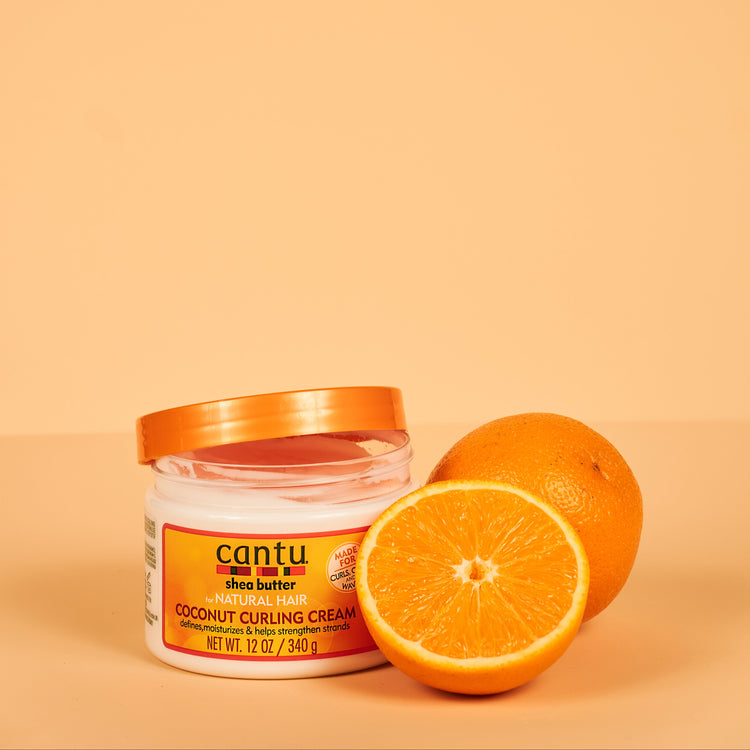 Cantu Shea Butter Coconut Curling Cream in een pot, omringd door natuurlijke ingrediënten zoals kokosolie en sheaboter.